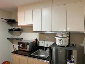una cocina con armarios blancos, fregadero y electrodomésticos en One Regis Bacolod- Upper East Studio Room en Bacólod