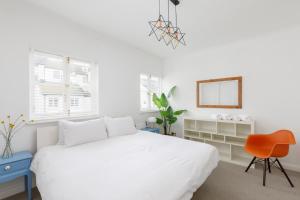 a white bedroom with a white bed and a orange chair at Beachfront Getaway 2-Bedroom House with FREE Private Parking & Patio in Brighton & Hove