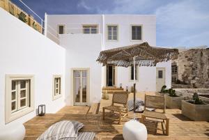 a white house with a patio with chairs and an umbrella at Niove Suites Milos in Plaka Milou