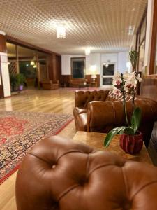 a living room with a leather couch and a table with flowers at Excelsior Hotel Cimone LowCost in San Martino di Castrozza