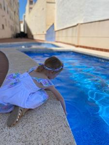 Una niña con un vestido sentada junto a una piscina en Apartment with solarium/terrace., en Calpe
