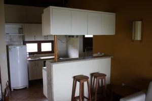a kitchen with two bar stools and white cabinets at Casa espetacular em condomínio pé-na-areia, RZ15 in Rio do Fogo