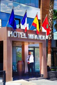 un homme debout devant un hôtel avec drapeaux dans l'établissement MIRANDA HOTEL - Tanger, à Tanger