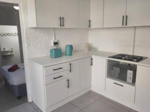 a white kitchen with white cabinets and a microwave at Cottage near Lagoon beach in Durban in Durban