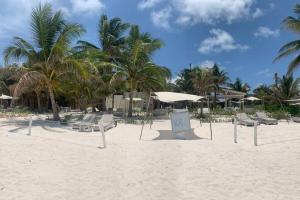 einen Sandstrand mit Liegestühlen, Sonnenschirmen und Palmen in der Unterkunft LUXURY CONDO EXCLUSIVE ¨ALDEA ZAMA¨ in Tulum