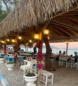 a restaurant with tables and chairs and a straw roof at Avlu Otel Palamutbükü in Datca