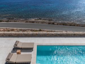 a swimming pool with two lounge chairs and the ocean at Myko Villa Private Heated Pool on beach in Ornos