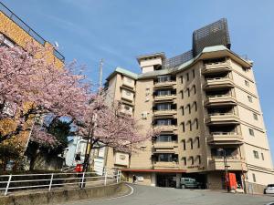wysoki budynek apartamentowy z kwitnącymi drzewami przed nim w obiekcie Hotel Kan-ichi w mieście Atami
