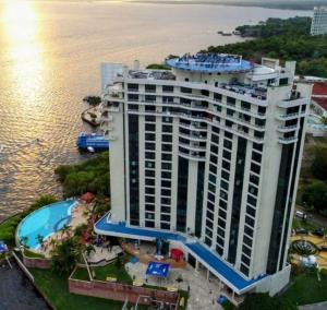 a large building with a swimming pool next to the water at Flat Hotel Tropical Executive Praia Ponta Negra in Manaus