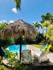 a straw umbrella and chairs next to a swimming pool at Villa TrÔpik Diamond + Bungalow in Le Diamant