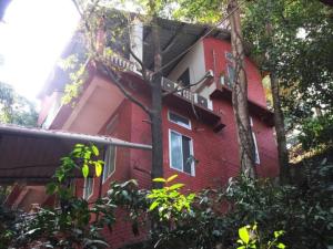 a red brick building with a balcony and trees at Hilltop Lodge in Guwahati