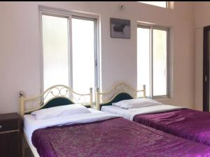two beds in a bedroom with two windows at Hilltop Lodge in Guwahati