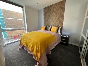 um quarto com uma cama com um edredão amarelo e uma janela em Ebony Apartments MK em Milton Keynes
