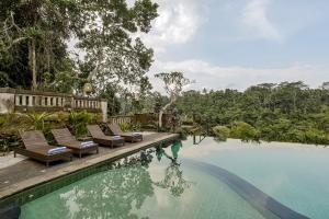 a swimming pool with chairs and trees in the background at Teja Lokha Ubud Villa in Ubud