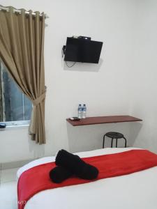 een slaapkamer met een bed met een rode deken en een televisie bij MURAI Guesthouse Bali in Denpasar