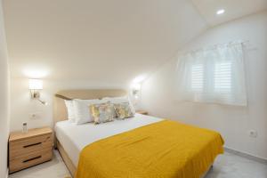 a white bedroom with a bed with a yellow blanket at Apartmani Vasiljević in Herceg-Novi
