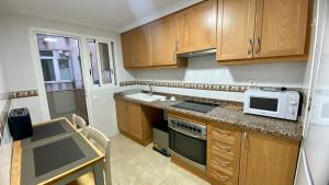 a small kitchen with wooden cabinets and a microwave at Amplio apartamento en centro in Denia