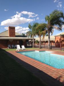 a swimming pool with two lawn chairs and palm trees at Philadelphia Motor Inn in Echuca