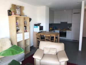 a living room with a white chair and a kitchen at One bedroom 3pieces entire Modern Appartment close to Airport, CERN, Palexpo, public transport to the center of Geneva in Meyrin