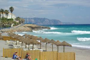 Grupa ludzi siedząca na plaży z parasolami w obiekcie Apartamento turístico Azahara w mieście Nerja