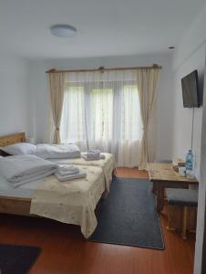 1 dormitorio con 2 camas, mesa y cortinas en Pensiunea Trei Brazi Arieseni en Arieşeni