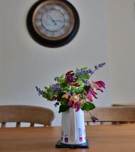 a vase filled with flowers on a table with a clock at Country Cottage with Far Reaching Views in Presteigne