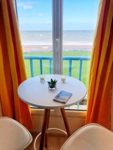 einen Tisch mit zwei Tassen und ein Buch neben einem Fenster in der Unterkunft Studio avec vue mer exceptionnelle sur la plage in Dieppe