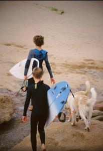 a man walking a dog on the beach with a surfboard at Onda Surf in Taghazout