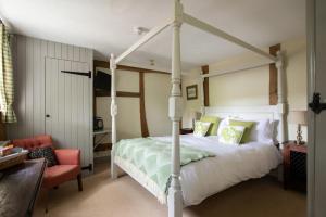 ein Schlafzimmer mit einem weißen Himmelbett und einem roten Stuhl in der Unterkunft The Griffin Inn in Fletching