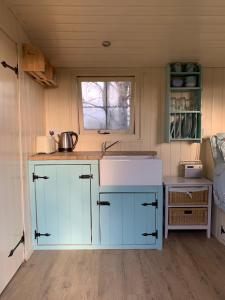 a small kitchen with blue cabinets and a sink at Delilah the shepherd's hut in Sidlesham