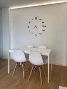 ein Tisch mit vier weißen Stühlen und einer Uhr an der Wand in der Unterkunft Torrenueva con vistas al mar in Torrenueva