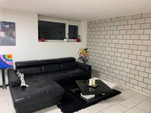 a black couch in a living room with a brick wall at Basel - 5 mins away - Modern Basement Studio with Kitchen 35m2 in Muttenz in Muttenz