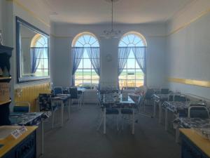 un comedor con mesas, sillas y ventanas en The Edenhurst Guesthouse, en Weymouth