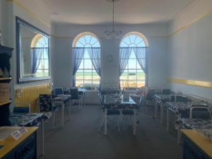 a dining room with tables and chairs and windows at The Edenhurst Guesthouse in Weymouth