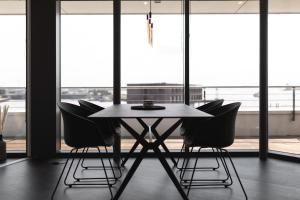 une table et des chaises dans une pièce avec fenêtres dans l'établissement Bheaven I Penthouse Premium Apartment, à Bremerhaven
