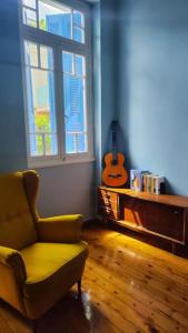 a living room with a chair and a window and a guitar at Yellow and blue relax house in Piraeus