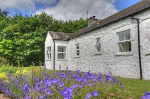 a stone house with purple flowers in front of it at Orroland Holiday Cottages in Dundrennan