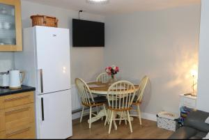 cocina con mesa, sillas y nevera blanca en The Snug At Kingfisher Cottage, en Antrim