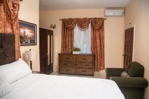 a bedroom with a bed and a chair and a window at Dela de-Rose Guest House Negril Jamaica in Negril