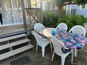 una mesa con sillas blancas y una mesa con un mantel colorido. en Mobile home camping en Le Grau-du-Roi