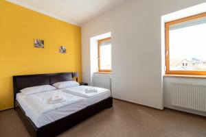 a bedroom with a bed with yellow walls and two windows at Hotel Prácheň in Horažďovice