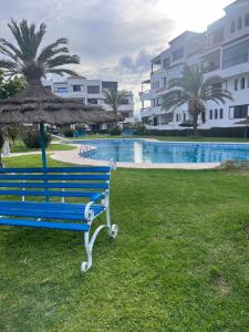 eine blaue Bank mit einem Regenschirm neben einem Pool in der Unterkunft Coin Confort 2 chambres de luxe avec piscine in Tétouan