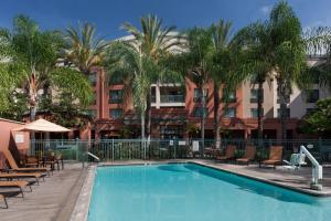 einen Pool in einem Hotel mit Stühlen und Palmen in der Unterkunft Courtyard Los Angeles Burbank Airport in Burbank