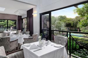 Protea Hotel by Marriott Midrand في ميدراند: مطعم بطاولات بيضاء وكراسي ونوافذ كبيرة