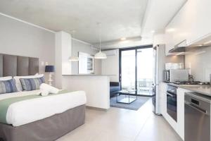 a white bedroom with a large bed and a kitchen at Lux Holiday Apartment Sibaya in Umdloti