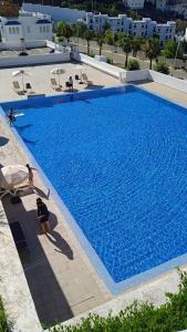 een groot blauw zwembad met mensen in stoelen ernaast bij Appartement résidence lilia al jabal M'diq in M'diq