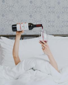 a woman laying in bed holding a glass of wine at The House Hotel Old Tbilisi in Tbilisi City