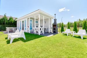 a white cottage with white chairs on the grass at Villa Polna in Grzybowo