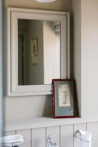 une image encadrée sur un comptoir de salle de bains avec un miroir dans l'établissement La Maison d’Hôtes, à Silly