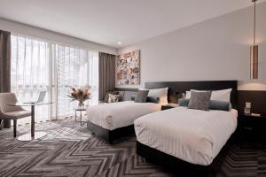 a hotel room with two beds and a desk and a table at Rydges Perth Kings Square in Perth